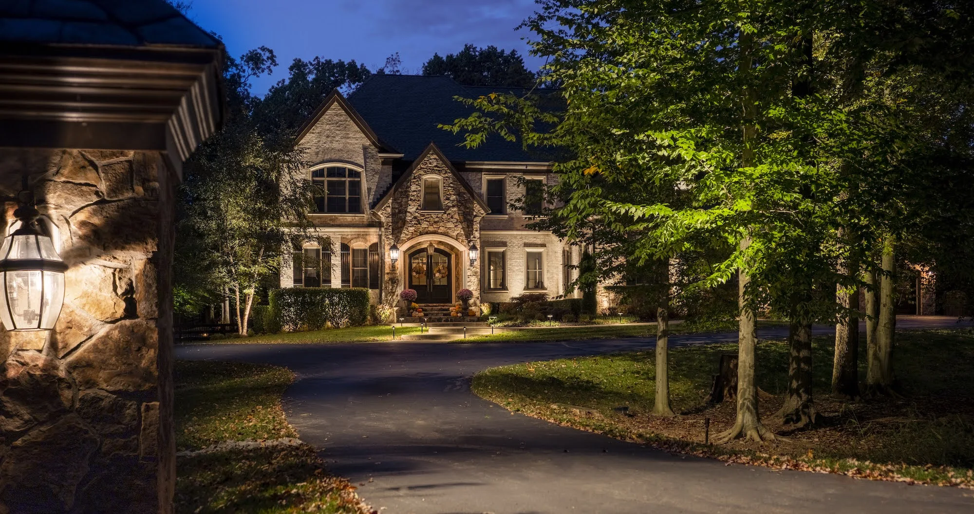 A large home front and yard showing the impact of landscape lighting for a before and after reveal.