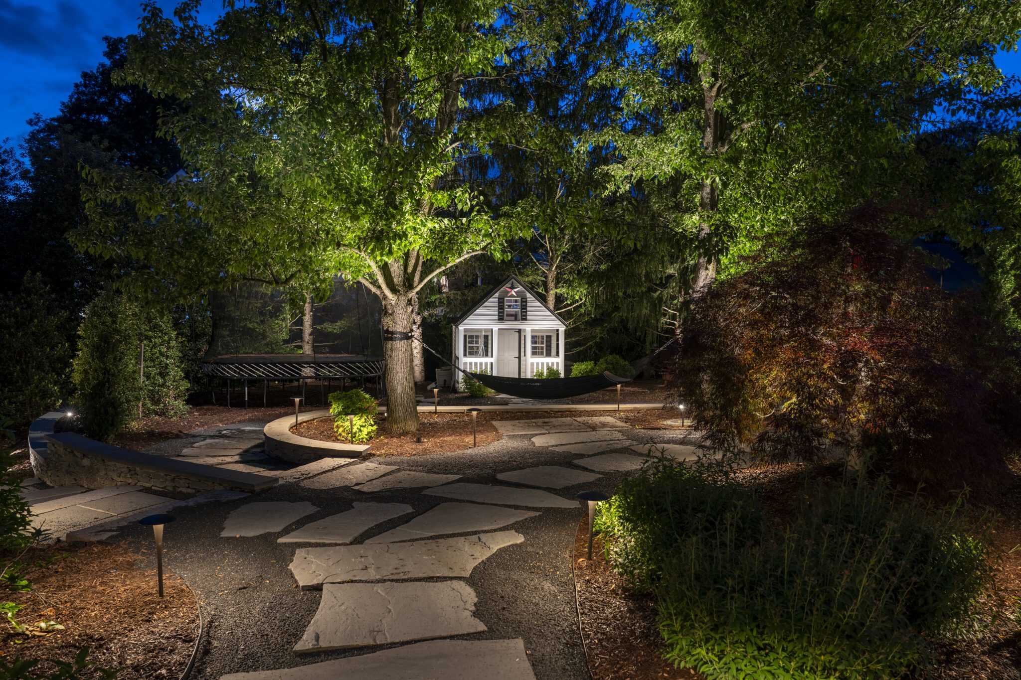 Flagstone path through a garden with an uplit shade tree and a small cottage beyond in Great Falls, VA