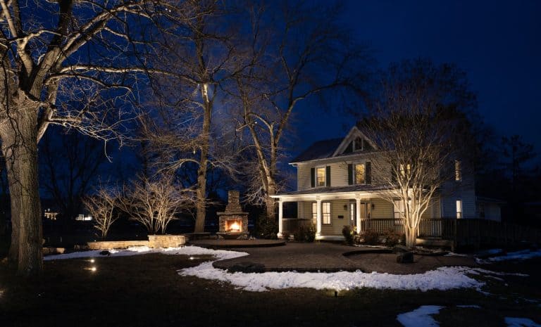 Dayloom office in Aldie, VA at night with a glowing outdoor stone fireplace, uplit bare trees, a lit porch and snow on the lawn
