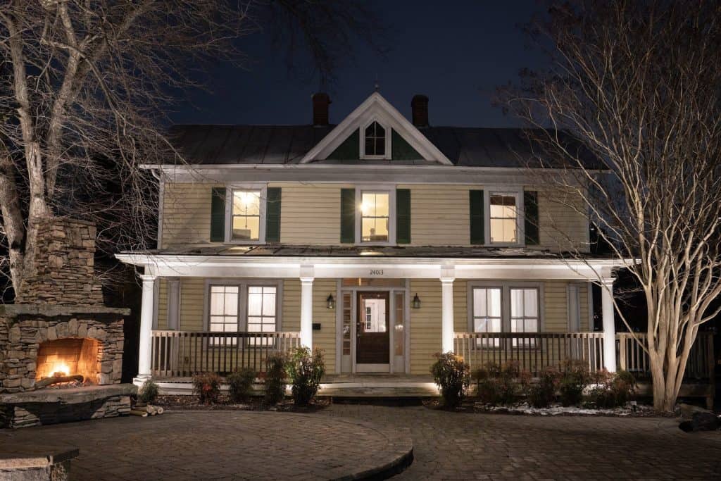Dayloom office in Aldie, Loudoun County, VA: farmhouse-style facade with lit porch columns, stone fireplace glow and garden lighting