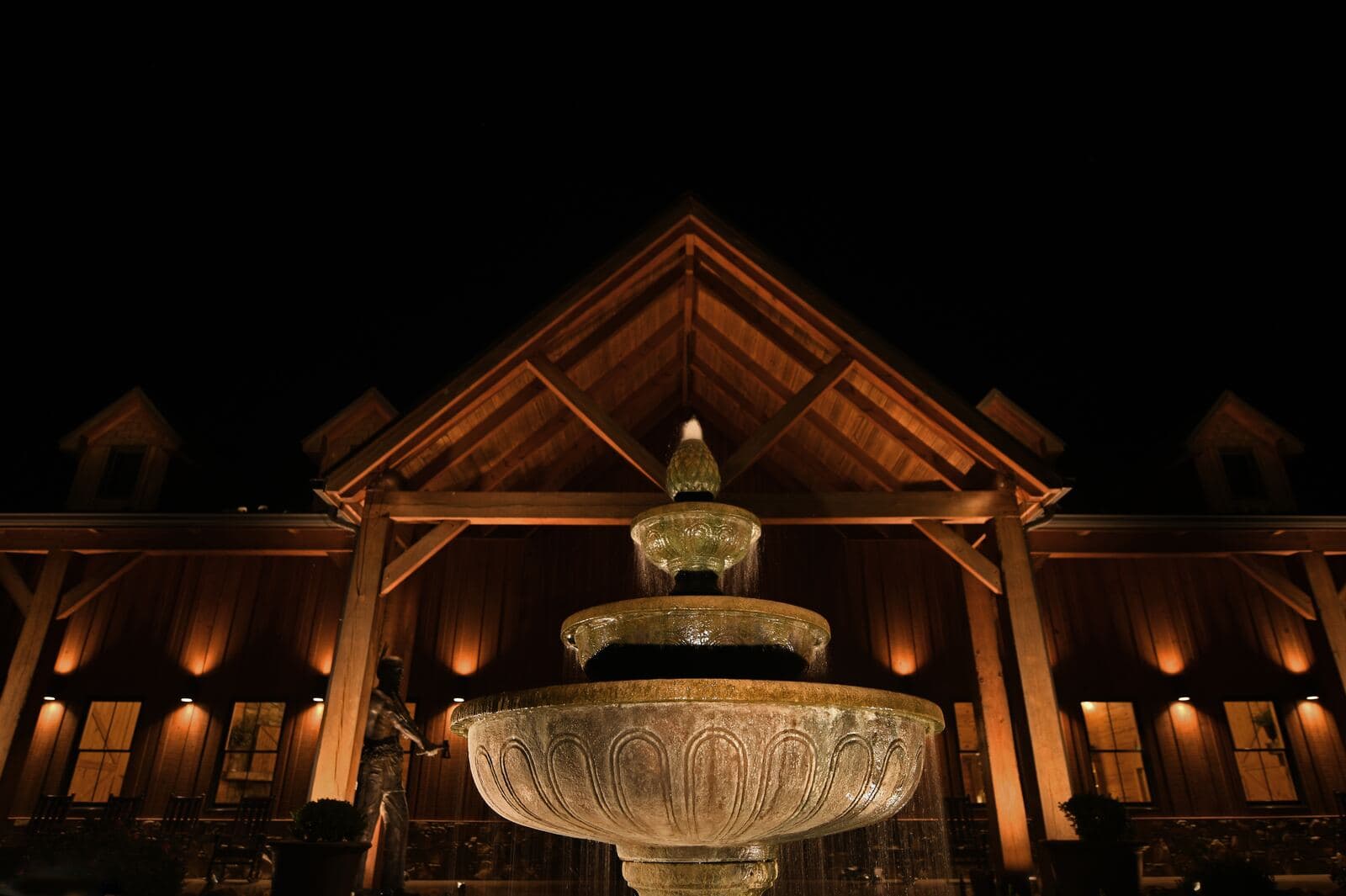 Timber-framed gable facade and tiered stone fountain softly illuminated with architectural lighting at night
