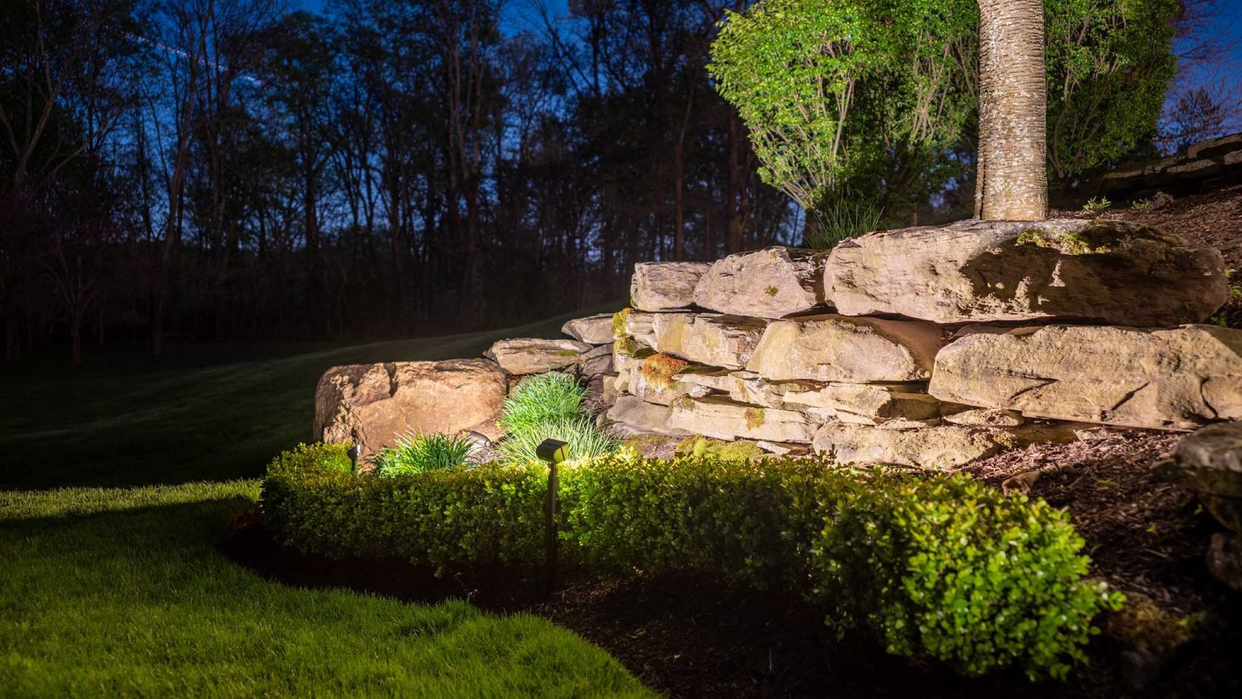 A stacked-stone retaining wall and plantings lit at night on a Loudoun County, VA property.