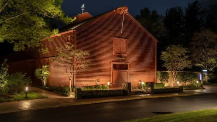 The Barns of Wolf Trap in Vienna, Virginia, at night, the red barn gable washed in warm light with uplit trees and garden beds