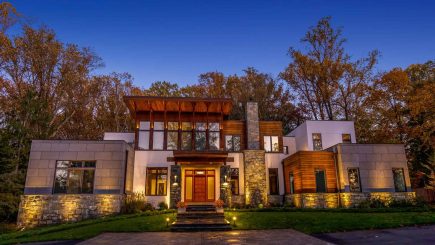 A modern home in McLean at dusk, with warm light on stone and glass walls, a lit terrace and uplit trees behind.